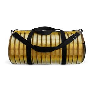 Puede incluir: Una bolsa de lona negra con un patrón de monedas de oro. La bolsa tiene una cremallera y dos correas ajustables.