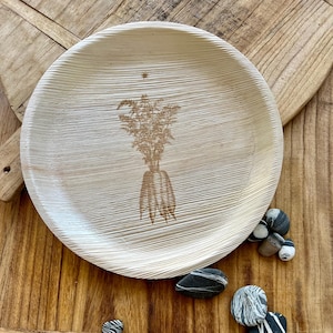 May include: A round, light-colored plate with a textured surface and a carved design of a plant with roots. The plate is made of natural material and is set on a wooden surface. Decorative pebbles are scattered around the plate.