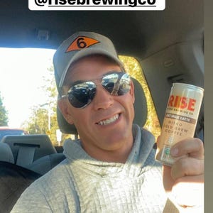 Puede incluir: Una persona sostiene una lata de RISE Oat Milk Latte Nitro Cold Brew Coffee. La lata es de color beige y blanco con el logotipo de RISE. La persona lleva un gorro gris y gafas de sol. El texto de la imagen dice "Much needed afternoon pick me up @risebrewingco".