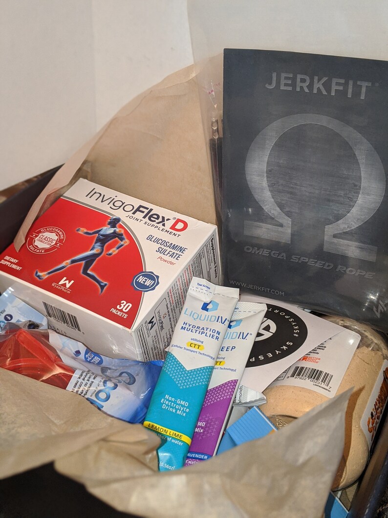 Puede incluir: Una caja llena de productos de salud y fitness. Los art&iacute;culos incluyen una caja de suplemento para las articulaciones InvigoFlex D, sobres de mezcla de hidrataci&oacute;n Liquid I.V. y una cuerda de velocidad JerkFit Omega. La caja est&aacute; forrada con papel marr&oacute;n.
