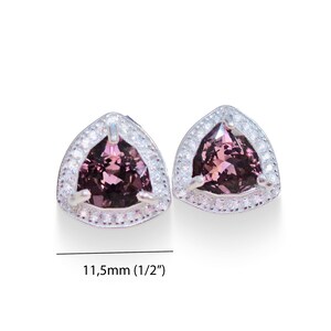 May include: A pair of silver earrings with a triangular shaped purple gemstone surrounded by a halo of smaller white gemstones. The earrings are 11.5mm (1/2") in size.