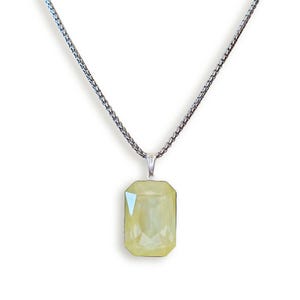 Op de afbeelding: Zilveren ketting met een rechthoekige, lichtgele hanger. De hanger heeft een facetgeslepen oppervlak dat het licht vangt. De ketting heeft een fijn, getextureerd ontwerp en de hanger is bevestigd met een kleine zilveren bale.
