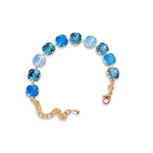 May include: A gold-toned bracelet featuring a series of square, blue crystal stones in varying shades. The bracelet has a chain-link design and a lobster clasp closure. The crystals range from light to deep blue.