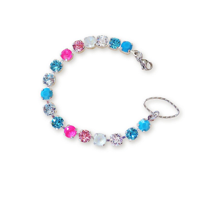 May include: A silver bracelet with a series of colorful, round gemstones. The gemstones are in shades of pink, blue, and clear, and are connected by a silver chain. The bracelet also has a small ring attached to it.