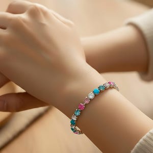 May include: A colorful bracelet with round gemstones in shades of turquoise, pink, and clear white. The bracelet is worn on a wrist, with the gemstones set in a silver-colored metal. The bracelet is a piece of jewelry.