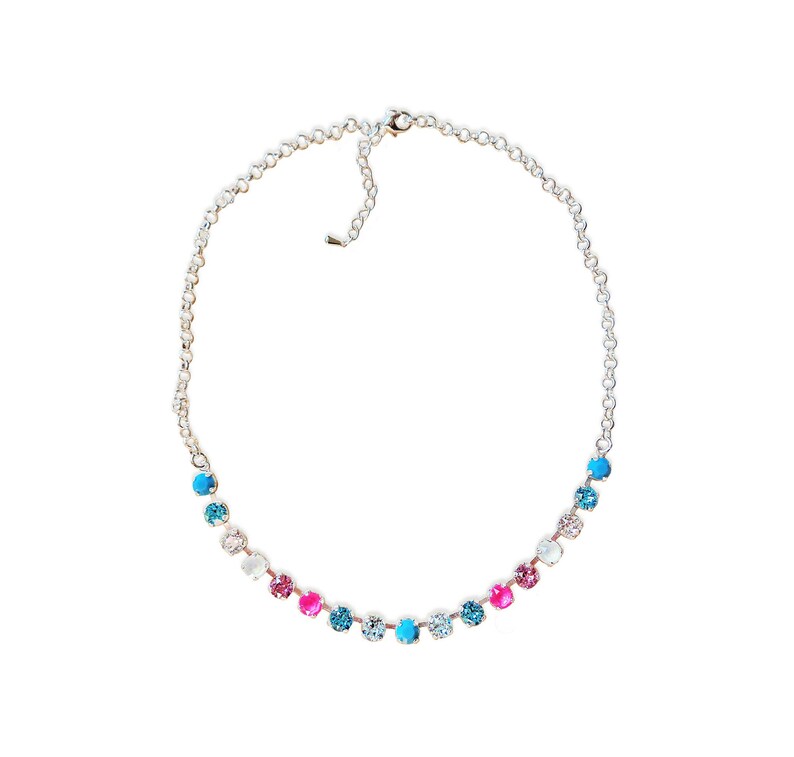May include: A silver-toned necklace featuring a series of colorful, round gemstones. The gemstones are arranged in a graduated pattern, with shades of pink, blue, and clear crystals. The necklace has a delicate chain and a secure clasp.