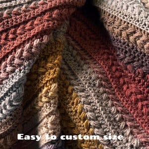 May include: Close-up of a handmade crochet blanket with a textured cable stitch design. The blanket features a gradient of colors, including shades of gray, brown, and gold. The text "Easy to custom size" is visible.
