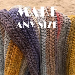 May include: A handmade, multi-coloured crochet blanket with the text "MAKE ANY SIZE" in white. The blanket features a textured stitch pattern and a gradient of colours, including grey, purple, brown, and gold. The blanket is folded over.