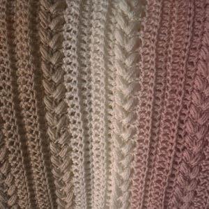 K&ouml;nnte beinhalten: Nahaufnahme einer handgefertigten H&auml;keldecke mit Farbverlauf. Die Decke geht von hellem Beige &uuml;ber Wei&szlig; zu einem zarten Rosa &uuml;ber. Das Design zeigt strukturierte vertikale Streifen mit komplizierten Stichmustern.