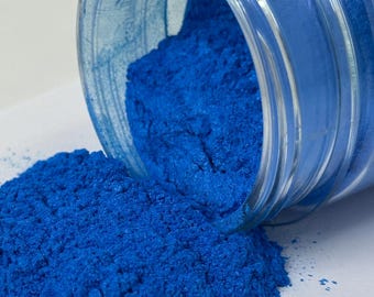 May include: A glass jar filled with a bright blue powder, spilling out onto a white surface.