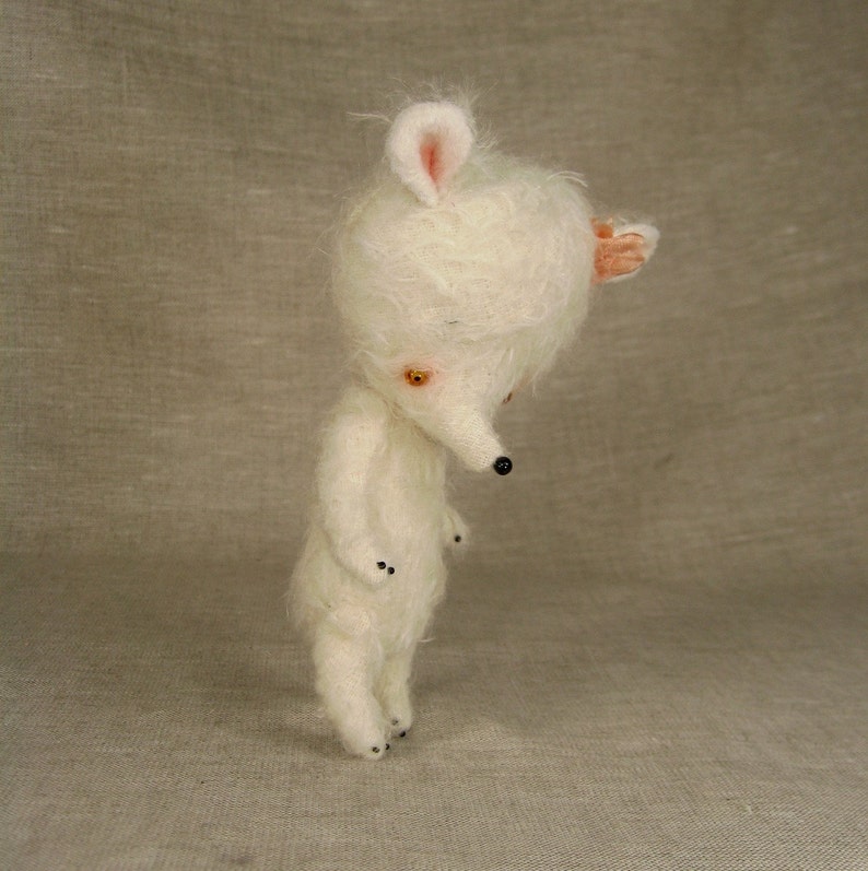 Puede incluir: Un juguete de peluche blanco con un hocico largo y orejas grandes. El juguete tiene ojos negros y una nariz negra. El juguete est&aacute; de pie sobre una superficie marr&oacute;n claro.