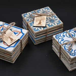 May include: Three sets of blue and white ceramic coasters with a floral and geometric design. Each set is tied with twine and a small wooden tag with a tree design and the word "Kamari" printed on it.