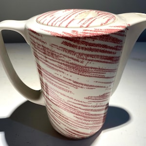 May include: A white ceramic coffee pot with a pink and white striped design. The pot has a lid and a handle.