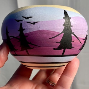 May include: A small, hand-painted ceramic pot with a purple, blue, and yellow sunset scene and black silhouette trees.