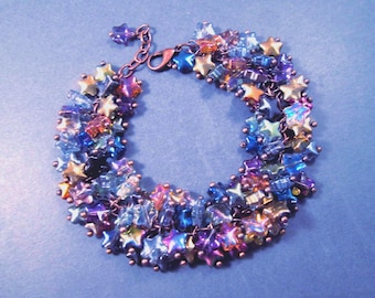 May include: A bracelet featuring a dense cluster of star-shaped beads in iridescent shades of blue, purple, and gold. The beads are linked together with copper-toned wire and small round beads, finished with a copper-toned lobster claw clasp.