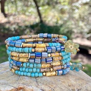 May include: A multi-strand beaded bracelet with turquoise, yellow, and blue beads. The bracelet is wrapped around a rock and has a flower charm.