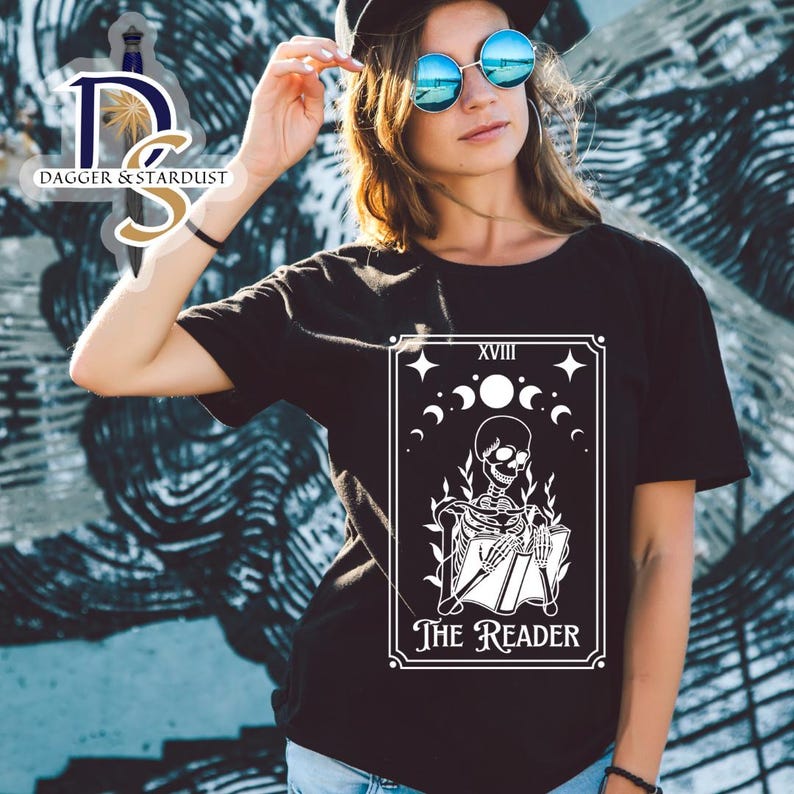 K&ouml;nnte beinhalten: Schwarzes T-Shirt mit einem wei&szlig;en Grafikdruck einer Tarotkarte. Die Karte ist "Der Leser", die 18. Karte der Gro&szlig;en Arkana. Die Karte zeigt ein Skelett, das ein Buch liest.