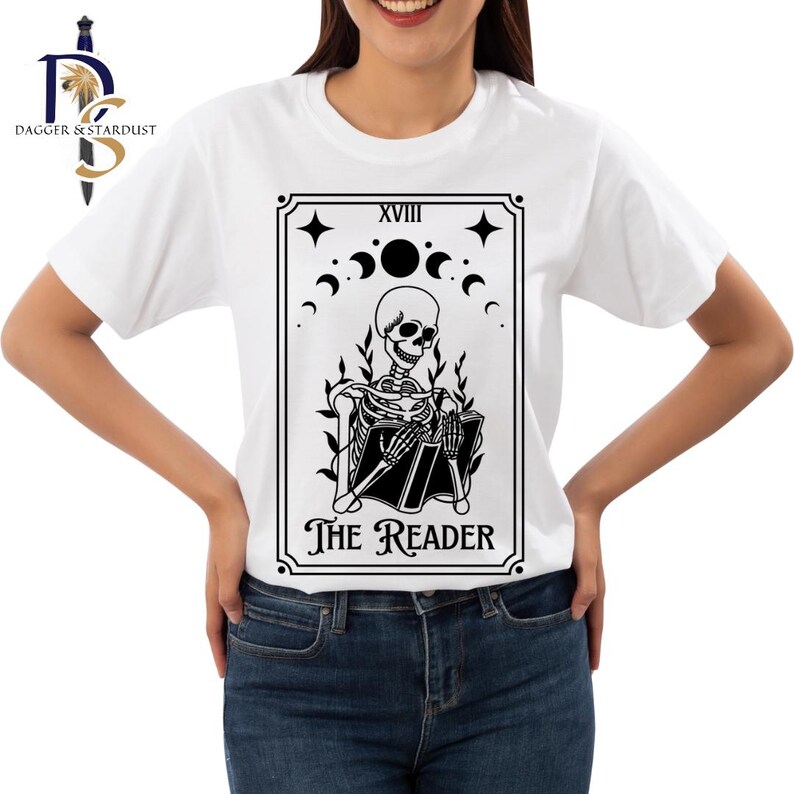 K&ouml;nnte beinhalten: Wei&szlig;es T-Shirt mit einer schwarz-wei&szlig;en Illustration einer Tarotkarte. Die Karte ist 'Der Leser', die 18. Karte der Gro&szlig;en Arkana. Die Karte zeigt ein Skelett, das sitzt und ein Buch liest.