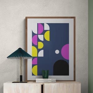 Può includere: Una stampa artistica astratta incorniciata con sfondo blu navy e forme geometriche gialle, rosa, bianche e nere. Una lampada verde e un bicchiere verde sono su un mobile in legno chiaro.
