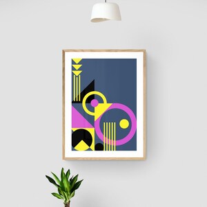May include: Abstract geometric art print in a wooden frame. The artwork features shapes in yellow, pink, black, and navy blue. A small potted plant and a decorative bowl sit on a grey chest of drawers below.