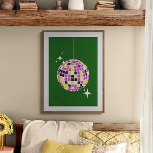 Könnte beinhalten: Ein gerahmter Druck einer Discokugel, die an der Decke vor einem grünen Hintergrund hängt. Die Discokugel ist lila, gelb und schwarz mit silbernen Akzenten. Auf dem grünen Hintergrund befinden sich zwei kleine weiße Sterne.