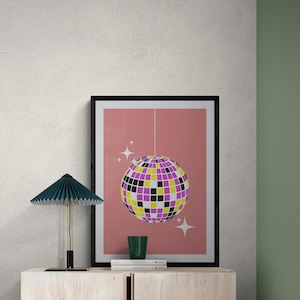 Puede incluir: Una impresión enmarcada de un fondo rosa con una bola de discoteca colgando del techo. La bola de discoteca está hecha de azulejos espejados en tonos de morado, amarillo y negro. Hay estrellas blancas alrededor de la bola de discoteca.