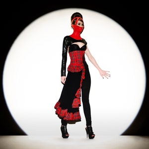 May include: A striking fashion ensemble featuring a red and black plaid corset, a black one-sleeve top, and a flowing black skirt with red plaid accents. The outfit is completed with black leggings, high heels, and a red face mask.