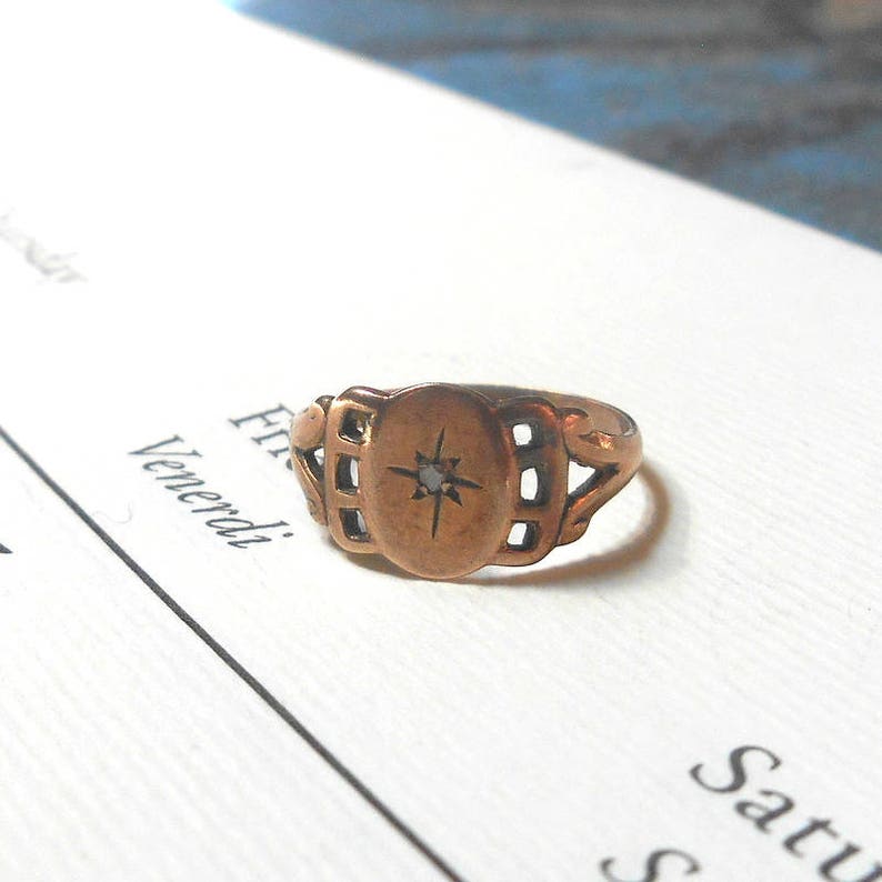 Puede incluir: Un anillo de oro con un engaste ovalado que presenta una peque&ntilde;a piedra transparente en el centro. El anillo tiene un dise&ntilde;o delicado e intrincado con detalles calados.
