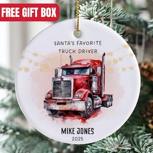 May include: A white ceramic Christmas ornament featuring a red semi-truck illustration. Text reads "SANTA'S FAVORITE TRUCK DRIVER" above the truck, with "MIKE JONES 2025" below. The ornament hangs from a gold string.