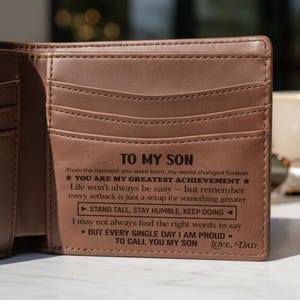 May include: Brown leather wallet with multiple card slots. The wallet has the text "TO MY SON" and a message from "LOVE, DAD" engraved on the front. The message includes the phrases "YOU ARE MY GREATEST ACHIEVEMENT" and "STAND TALL, STAY HUMBLE, KEEP GOING".