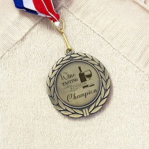 Könnte beinhalten: Bronzefarbene Medaille mit Lorbeerkranz-Design und der Aufschrift "Wine Tasting Kennedy Champion". Die Medaille hängt an einem rot-weiß-blauen Band. Die Medaille zeigt eine Grafik einer Weinflasche und eines Weinglases.