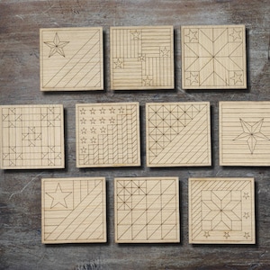May include: A collection of ten square wooden coasters with various geometric and star designs etched into the surface. The coasters are arranged on a dark wooden surface, showcasing the natural wood grain and intricate patterns.
