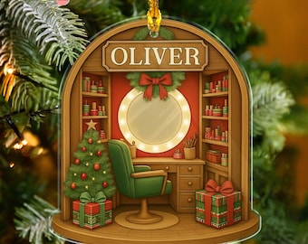 May include: A Christmas ornament featuring a salon scene with the name "OLIVER" above. The ornament includes a Christmas tree, a green chair, a mirror, and shelves filled with beauty products. A gift box with a red bow is also present.