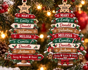 Op de afbeelding: Twee kerstboomvormige ornamenten bestaande uit gestapelde houten planken met de namen Mary, Emily, Donald, Valentina, Melissa, Camila, Daniella, Jackson, Sassy, Kason en Dozer, bekroond met een ster met het jaartal 2026 en rode linten.
