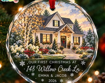 Puede incluir: Un adorno navideño redondo de cristal facetado con una ilustración de una casa al atardecer con nieve y árboles. El texto dice: OUR FIRST CHRISTMAS AT 148 Willow Creek Ln, EMMA & JACOB, 2026. Incluye una cinta roja para colgar.