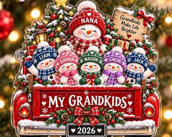 Op de afbeelding: Een kerstornament in de vorm van een rode pick-up laadbak met vijf sneeuwpoppen in kleurrijke mutsen en sjaals. De sneeuwpoppen zijn gelabeld met Nana, Liam, Sophia, Mason, Chloe en Jack. Een bord toont de tekst My Grandkids en 2026.