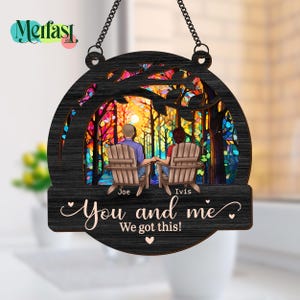 May include: A black wooden sign with a chain for hanging. The sign features a colorful forest scene with two figures in chairs, holding hands. Text reads "You and me, We got this!" and includes the names "Joe" and "Ivis".