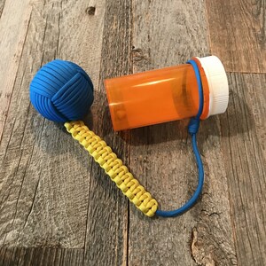 May include: A blue and yellow paracord keychain with a blue knotted ball and an orange pill bottle attached.