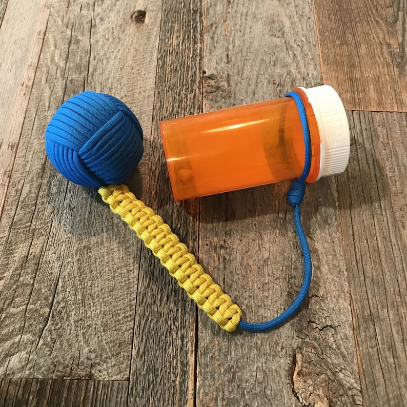 May include: A blue and yellow paracord keychain with a blue knotted ball and an orange pill bottle attached.