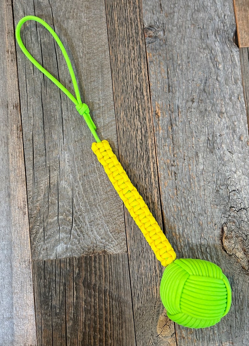 May include: A yellow and green paracord dog toy with a knotted ball at the end and a loop handle.