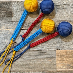 May include: Three knotted rope balls with attached cords. The balls are yellow, blue, and blue. The cords are red, blue, and yellow.