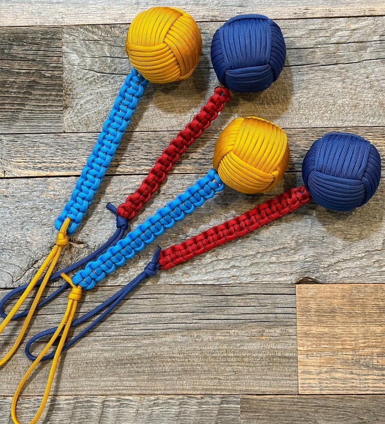 May include: Three knotted rope balls with attached cords. The balls are yellow, blue, and blue. The cords are red, blue, and yellow.