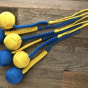 May include: Five blue and yellow paracord balls with a braided cord attached to each. The balls are made of paracord and are tied in a knot.