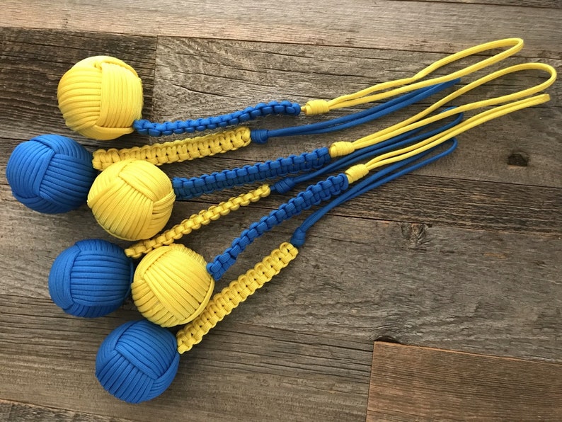 May include: Five blue and yellow paracord balls with a braided cord attached to each. The balls are made of paracord and are tied in a knot.