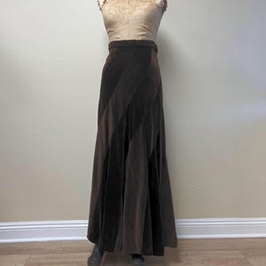 May include: A vintage-style ensemble on a mannequin. The outfit includes a tan top with lace detailing and a long, dark brown velvet skirt with diagonal panels. The skirt is floor-length, creating a flowing silhouette.