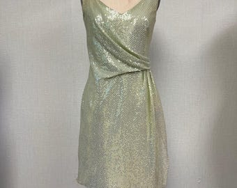 May include: A vintage, knee-length dress on a mannequin. The dress is covered in shimmering, pale green sequins. It features a V-neckline and a draped, asymmetrical design at the waist. The dress is sleeveless and has a classic, elegant silhouette.