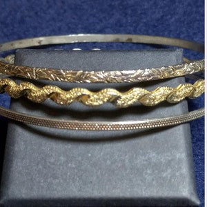 Puede incluir: Tres pulseras de plata, una con un diseño texturizado, otra con un diseño ondulado y otra con un diseño floral.