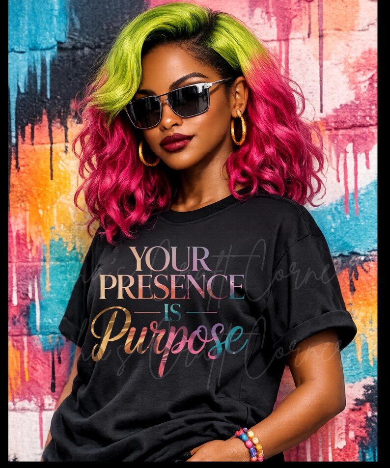 以下が含まれることがあります： カラフルなグラデーションで「YOUR PRESENCE IS PURPOSE」という文字がプリントされた黒いTシャツ。画像に写っている人物は、ピンクとグリーンの髪、サングラス、ゴールドのフープイヤリングをしています。手首にはカラフルなブレスレットがあります。