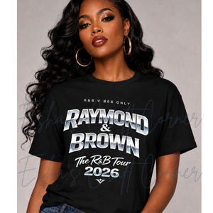 May include: Black t-shirt with the text "RAYMOND & BROWN The R&B Tour 2026" in a silver and white design. The shirt also has the text "R&B V BES ONLY" at the top. The model is wearing blue jeans and gold hoop earrings.