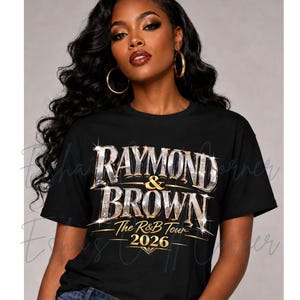 May include: Black t-shirt with the text "RAYMOND & BROWN - The R&B Tour - 2026" in a sparkling, metallic design. The shirt is worn by a person with long, dark hair and gold hoop earrings.